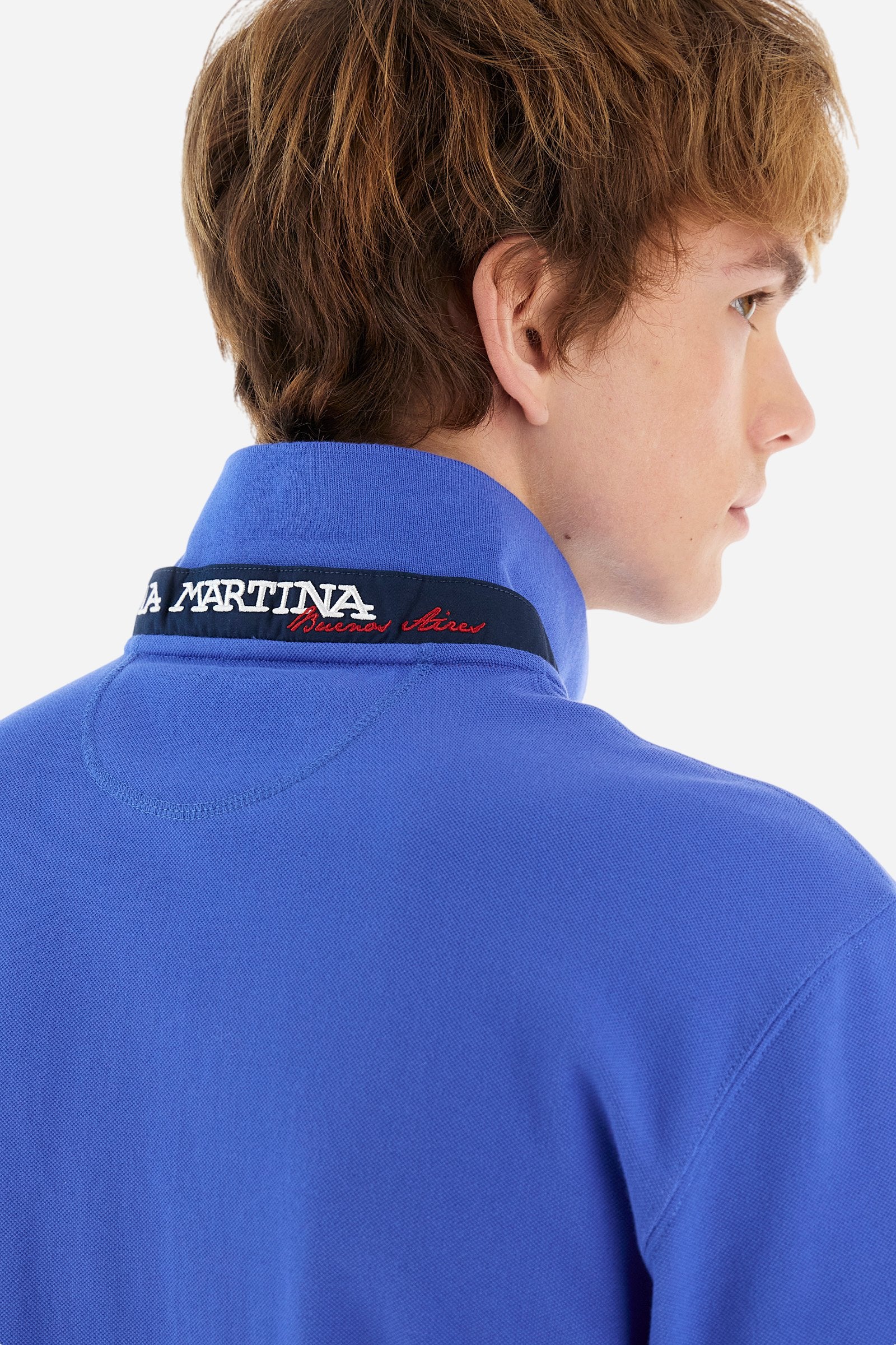 Men's plain short-sleeved polo shirt made from stretch piqué. Two-button fastening. The collar and cuffs are made from tone-on-tone ribbed fabric. Under the collar, there is a contrasting fabric panel with embroidered multicoloured lettering. The logo is embroidered on the left side of the chest in contrasting thread. Slim fit. The model is wearing a size L. - Dazzling Blue