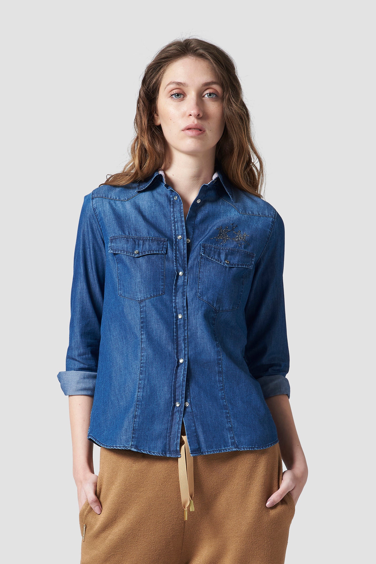 Women's plain-coloured, long-sleeved shirt in soft stretch cotton fabric featuring a classic cutaway collar. The classic fit is suitable for any figure as it remains relaxed and not too tight. Rhinestone La Martina logo on the front. Perfect for wearing with a pair of the collection's jeans or elegant trousers, day or night. The model is 174 cm tall and wearing a size S. - Medium Indigo Denim