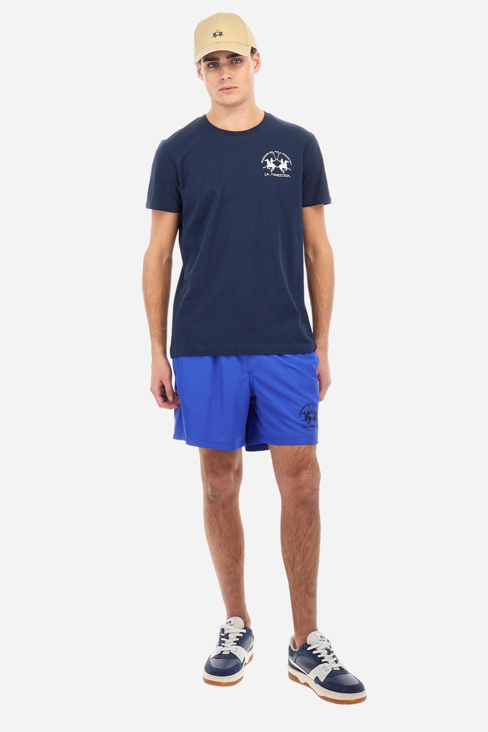 Plain men's swimming shorts made of nylon. Elastic waistband with a personalised drawstring for waist adjustment. On the inside of the shorts is an elasticated mesh brief. Double side pocket on the hips and patch pocket with flap on the back, on the right side only. The large logo is embroidered in a contrasting colour thread on the bottom of the left leg on the front. Regular fit. The model is wearing a size L. - Dazzling Blue