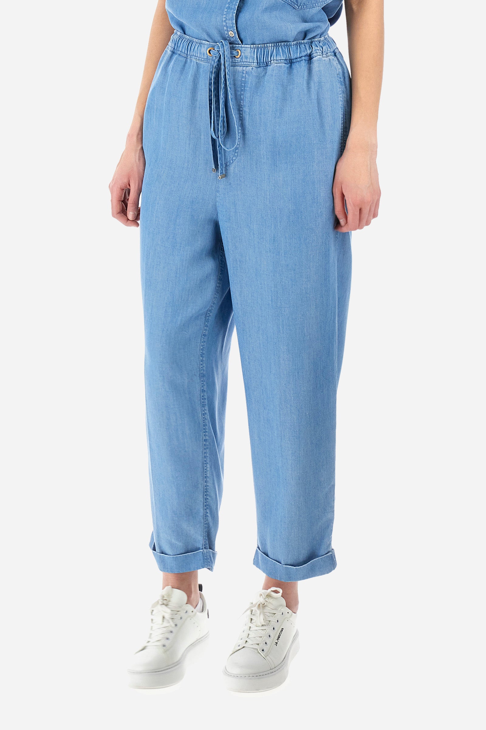 Women’s trousers in solid color, made of ecological lyocell denim fabric. Drawstring waist and laces to adjust the closure comfortably. Two front and two back pockets, all flush. The logo is present on a patch sewn on the back and on a metal plate on the front. The fit is regular. The model wears a size 2. - Medium Indigo Denim