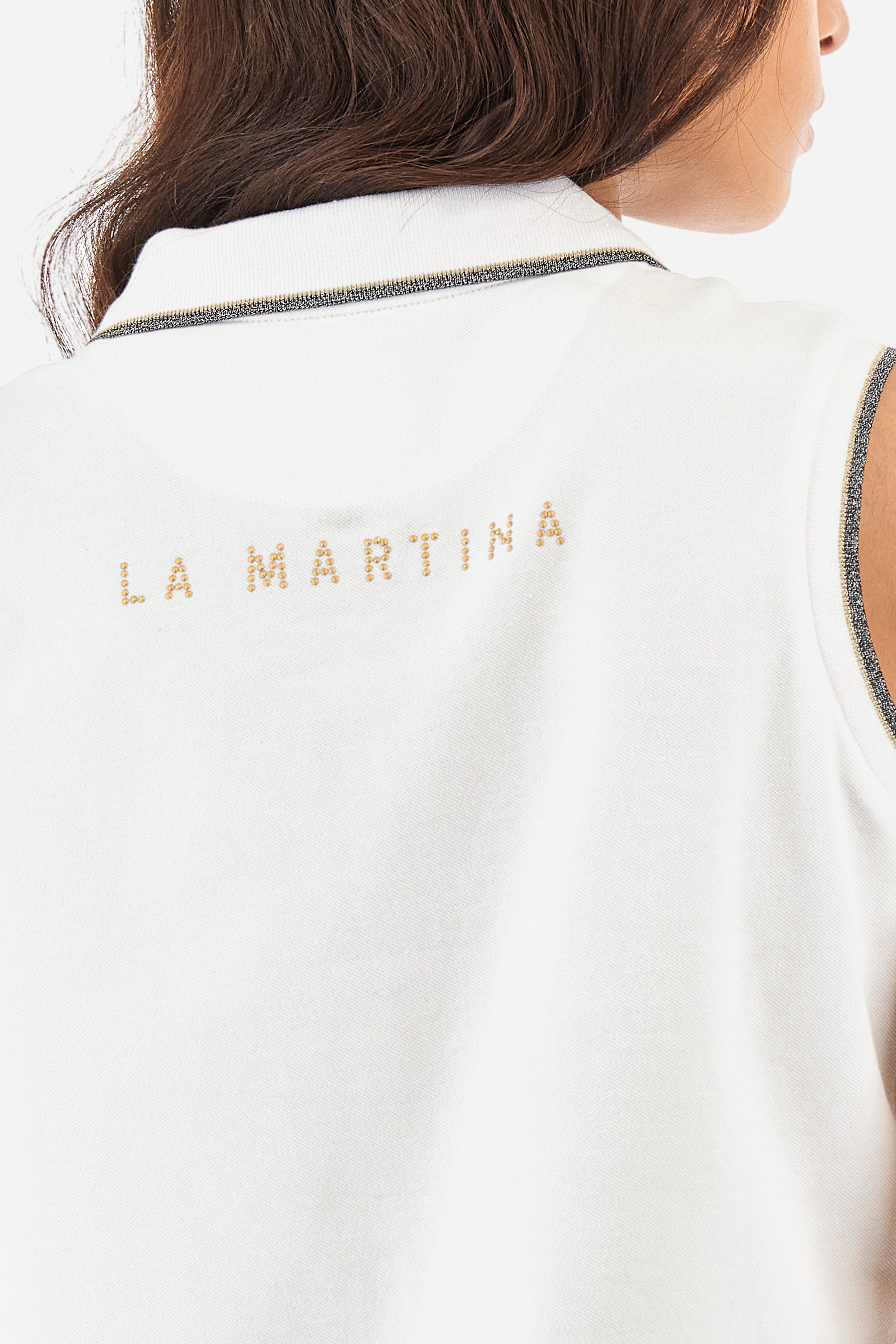 Women’s sleeveless polo shirt in solid color, made of stretch cotton. V-neck and 2 button closure. Collar and crew sleeves profiled and ribbed. Side slits. On the back there is the inscription "La Martina" composed of small rhinestones. The logo is present on the front. The fit is regular. The model wears a size 2 . - Optic White