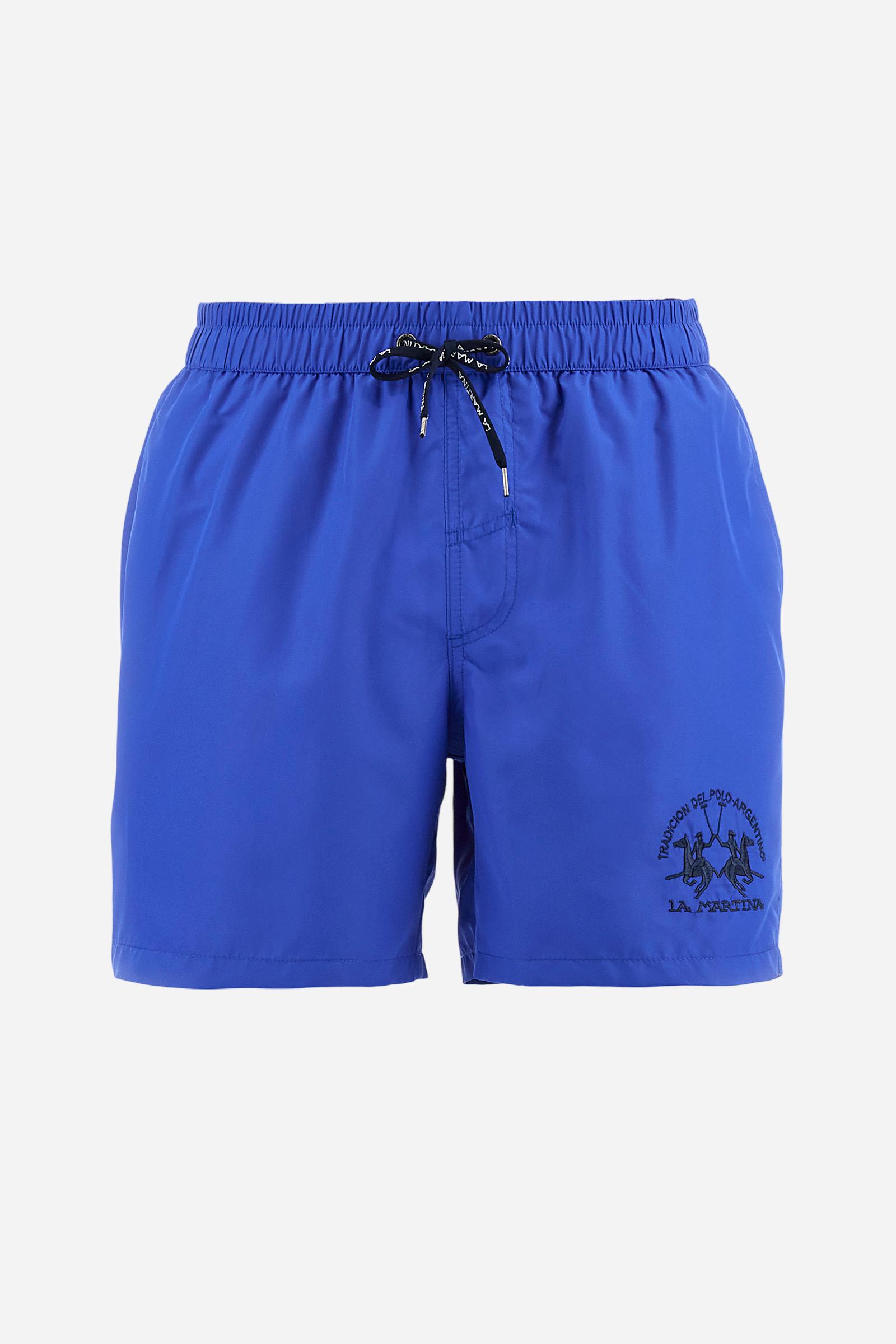 Plain men's swimming shorts made of nylon. Elastic waistband with a personalised drawstring for waist adjustment. On the inside of the shorts is an elasticated mesh brief. Double side pocket on the hips and patch pocket with flap on the back, on the right side only. The large logo is embroidered in a contrasting colour thread on the bottom of the left leg on the front. Regular fit. The model is wearing a size L. - Dazzling Blue