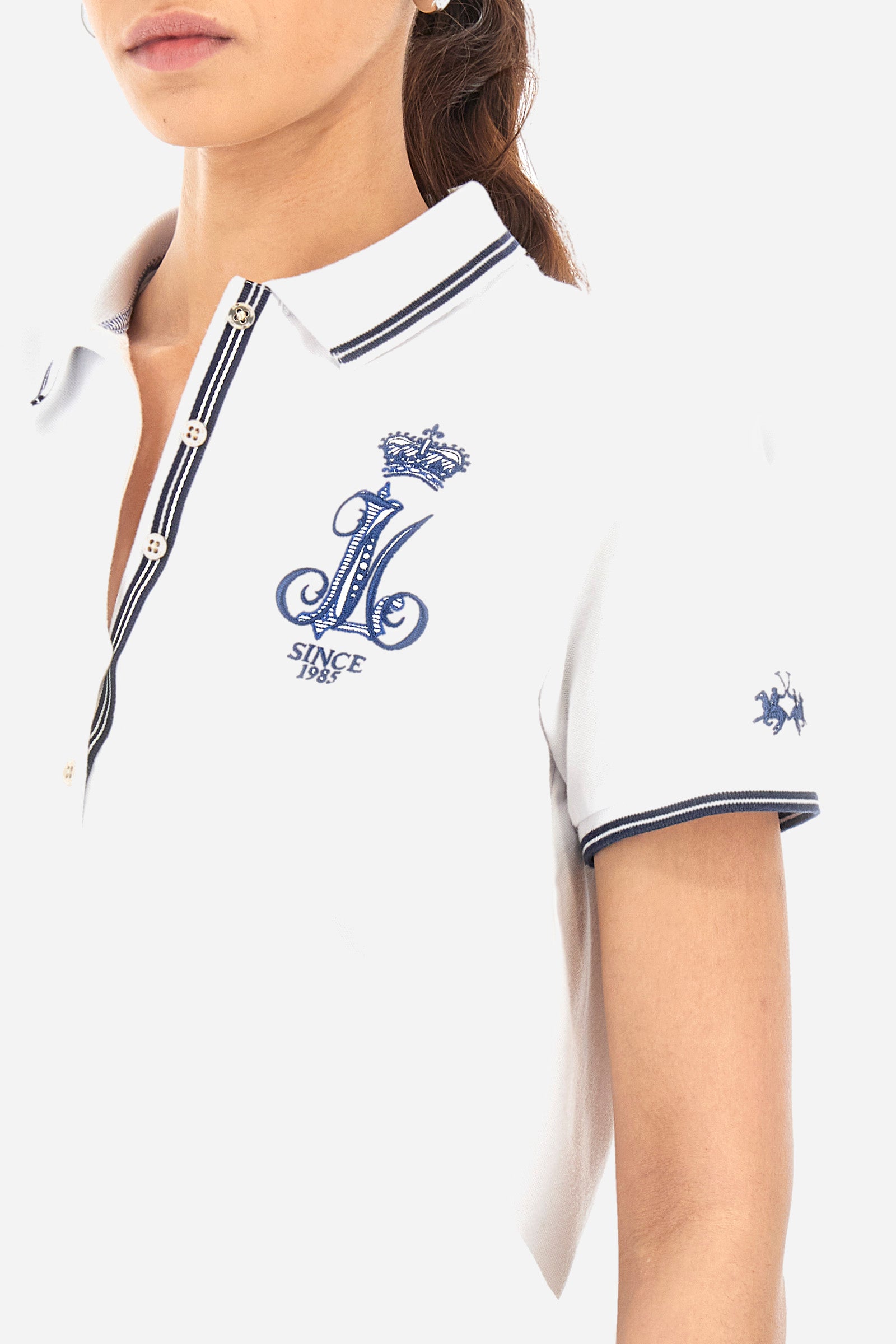Women’s polo with short sleeves in solid color, made of stretch cotton. 5-button closure, ribbed collar and crew sleeves, where contrasting stripes are sewn. Side slits. On the front are embroideries with symbols and initials of the brand, recalling the capsule collection Polo Club Grand Hotel. The logo is embroidered on a contrasting sleeve. The fit is regular. The model wears a size 2. - Optic White