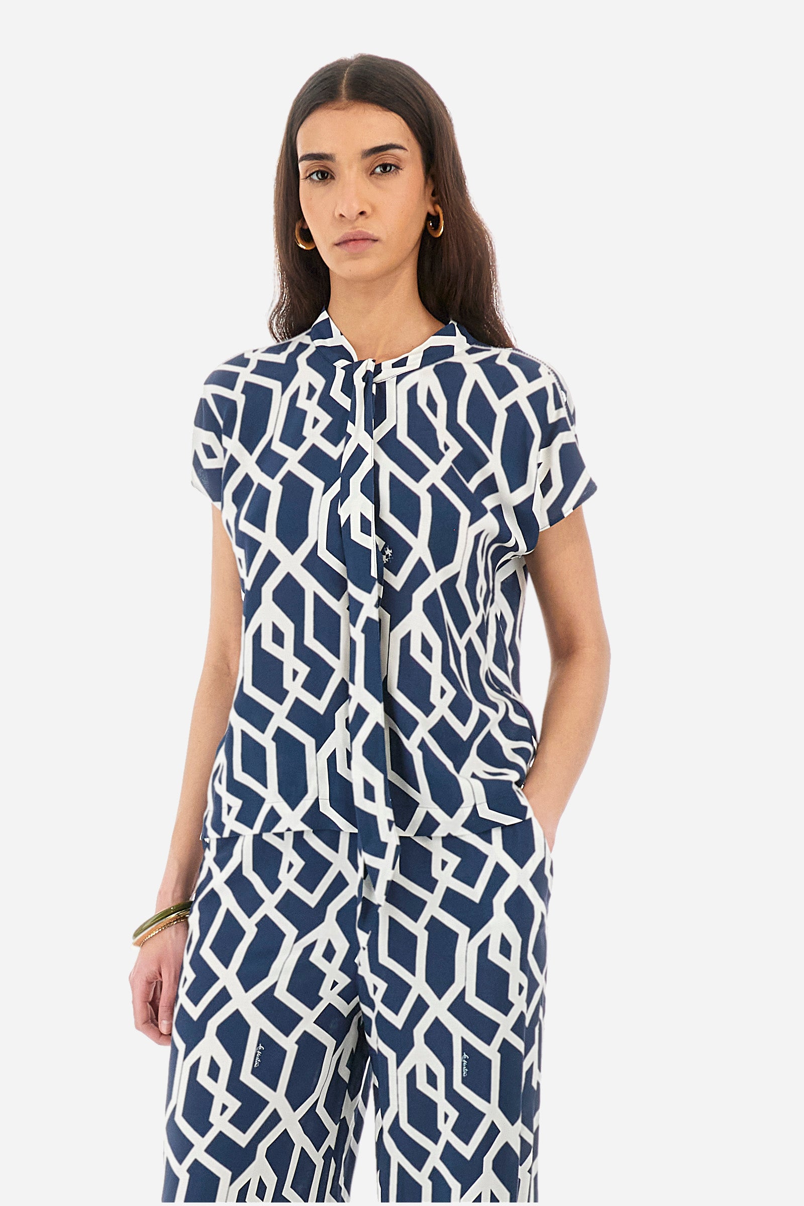 Women's short-sleeved blouse with a geometric print, made of synthetic fabric. A shawl collar. A small logo is present on a metal plate applied to the front and printed on the collar tie. The fit is regular. The model wears a size 2. - Orion blue/Off white