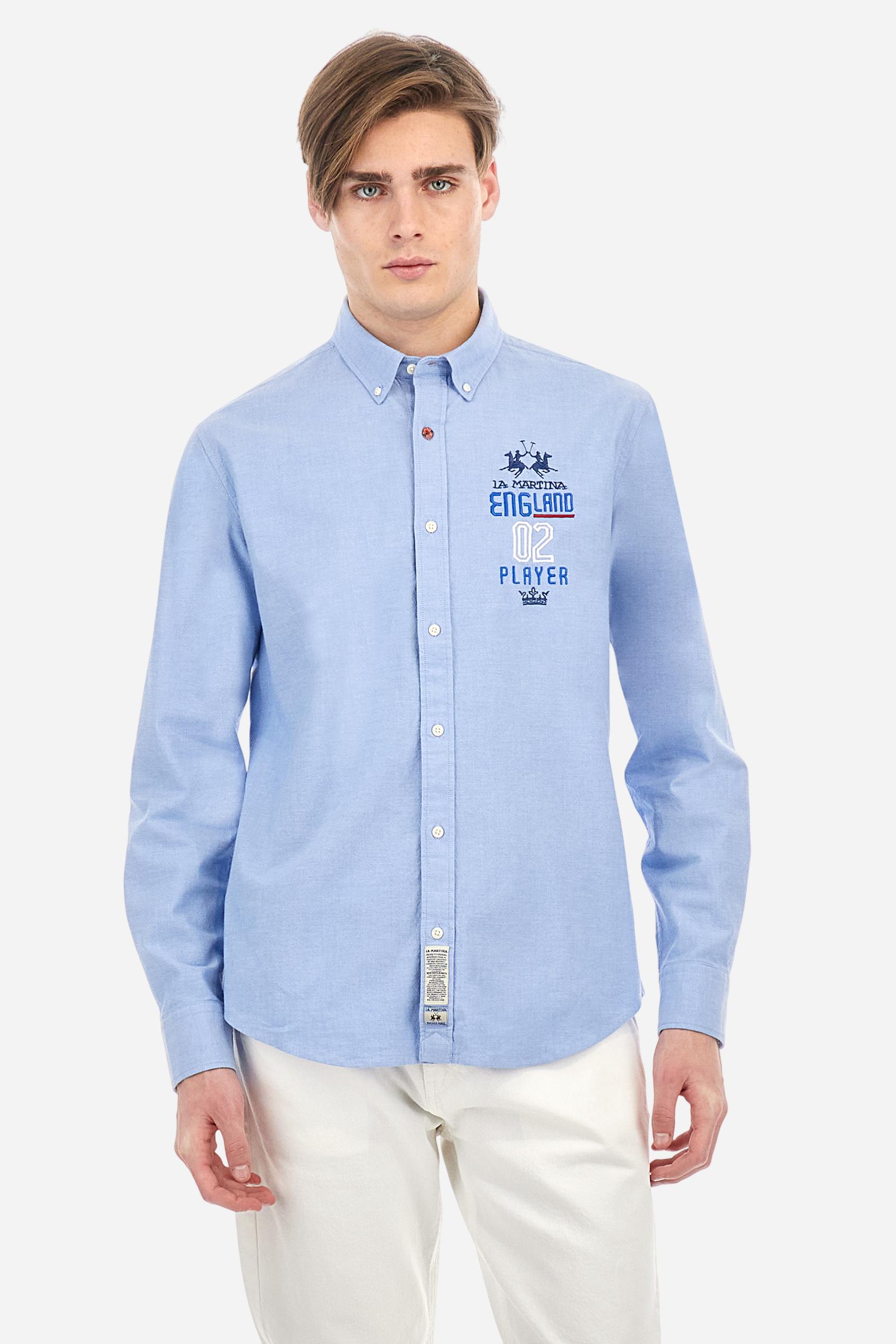 Men's long-sleeved plain shirt made from 100% Oxford cotton. The button-down collar is finished with a second button printed with the English flag. The multicoloured embroidery on the chest, over the heart, includes lettering, numbers and the logo, which add a distinctive touch. Regular fit. The model is wearing a size L. - Cornflower blue
