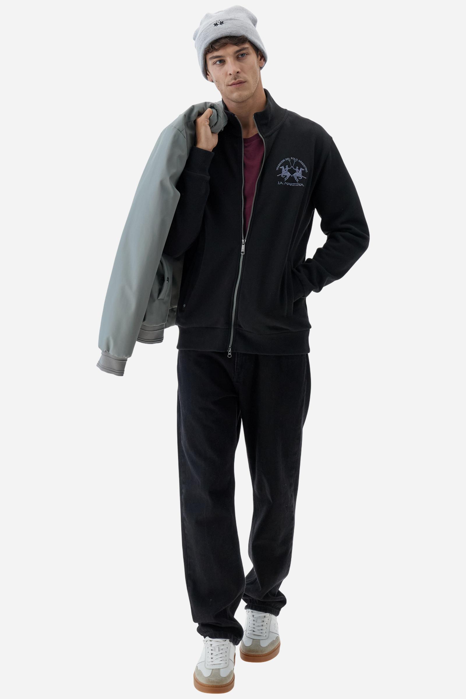 Men's long-sleeved solid colour sweatshirt. It is made of comfortable 100% cotton fleece with a soft-brushed feel. Model with high ribbed neck and front zip opening. Solid colour ribbed cuffs and waistband. The large contrasting brand team logo is embroidered on the chest. A contrasting colour fabric number patch is applied to the right sleeve. The model has a regular fit that offers a comfortable, relaxed silhouette. The model is wearing a size L. - Black