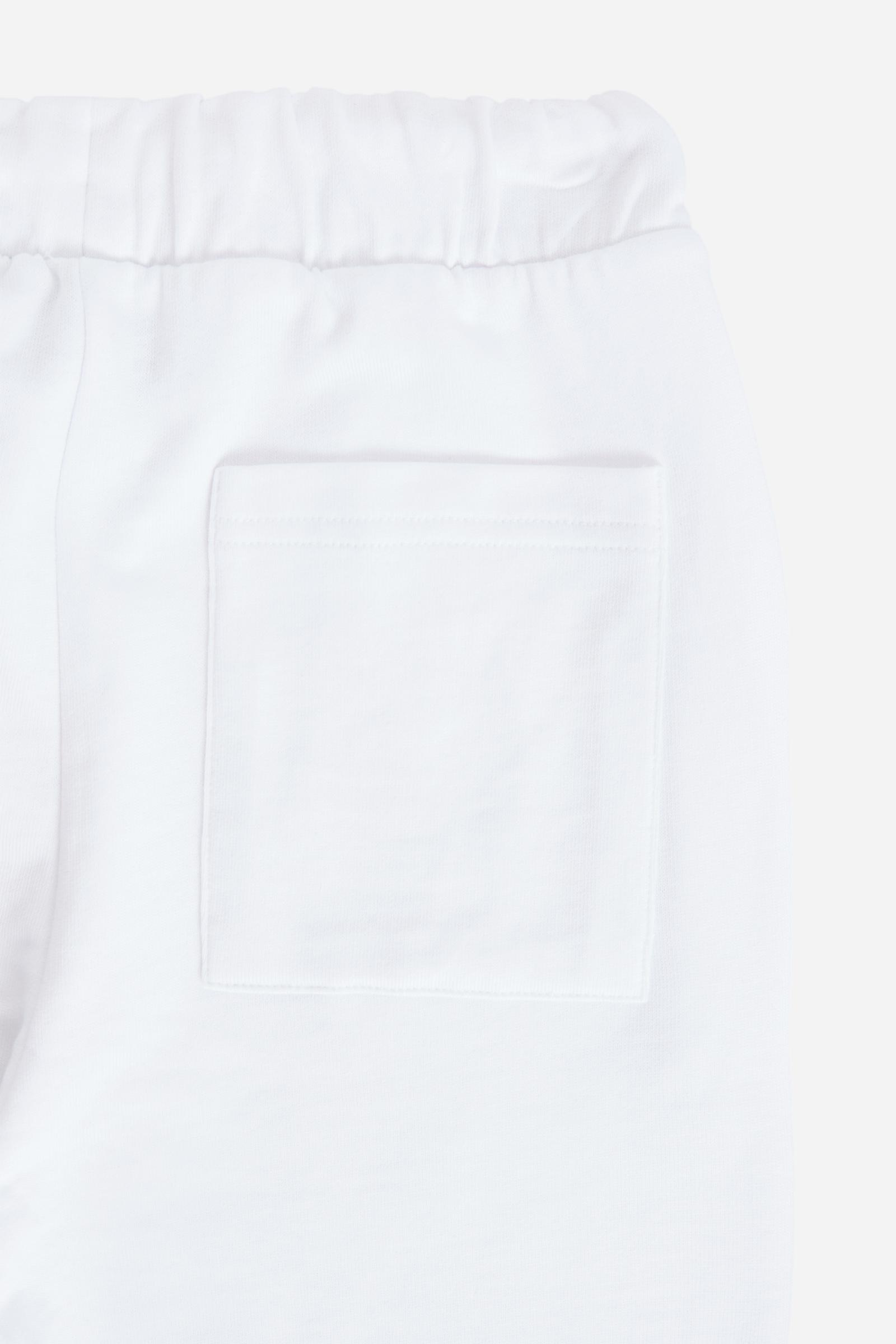 Bermuda shorts for boys made from soft 100% cotton fleece in a solid colour. The style features a clean, essential design, with an elasticated waist adjustable by drawstring and practical side pockets. A patch pocket is placed on the back, while the contrast embroidered maxi logo at the leg hem adds a distinctive and recognisable detail. A comfortable, versatile garment, ideal for leisure time. - Optic White