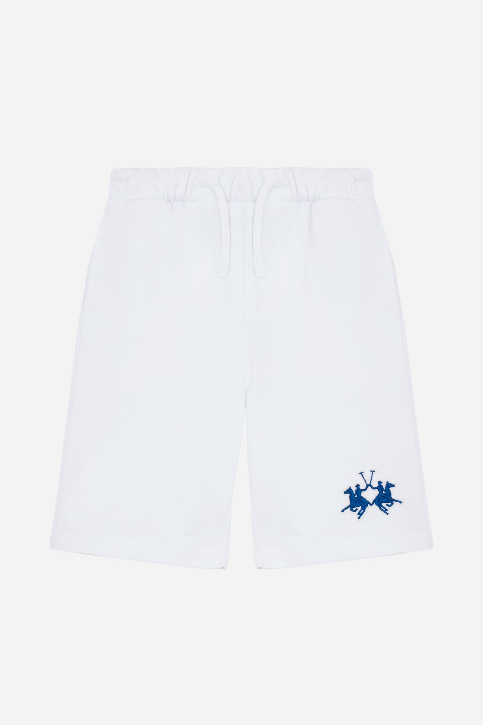 Bermuda shorts for boys made from soft 100% cotton fleece in a solid colour. The style features a clean, essential design, with an elasticated waist adjustable by drawstring and practical side pockets. A patch pocket is placed on the back, while the contrast embroidered maxi logo at the leg hem adds a distinctive and recognisable detail. A comfortable, versatile garment, ideal for leisure time. - Optic White