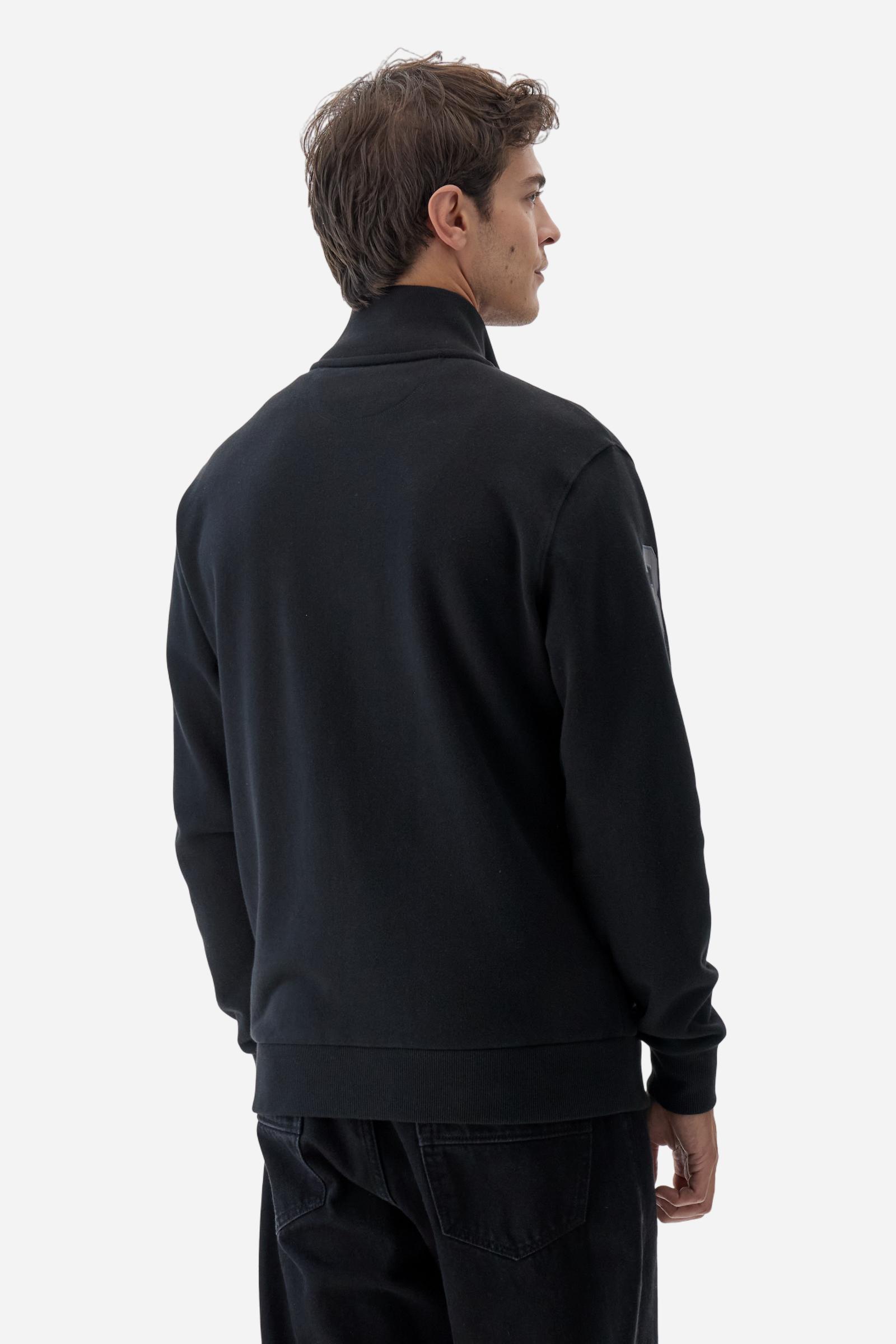 Men's long-sleeved solid colour sweatshirt. It is made of comfortable 100% cotton fleece with a soft-brushed feel. Model with high ribbed neck and front zip opening. Solid colour ribbed cuffs and waistband. The large contrasting brand team logo is embroidered on the chest. A contrasting colour fabric number patch is applied to the right sleeve. The model has a regular fit that offers a comfortable, relaxed silhouette. The model is wearing a size L. - Black