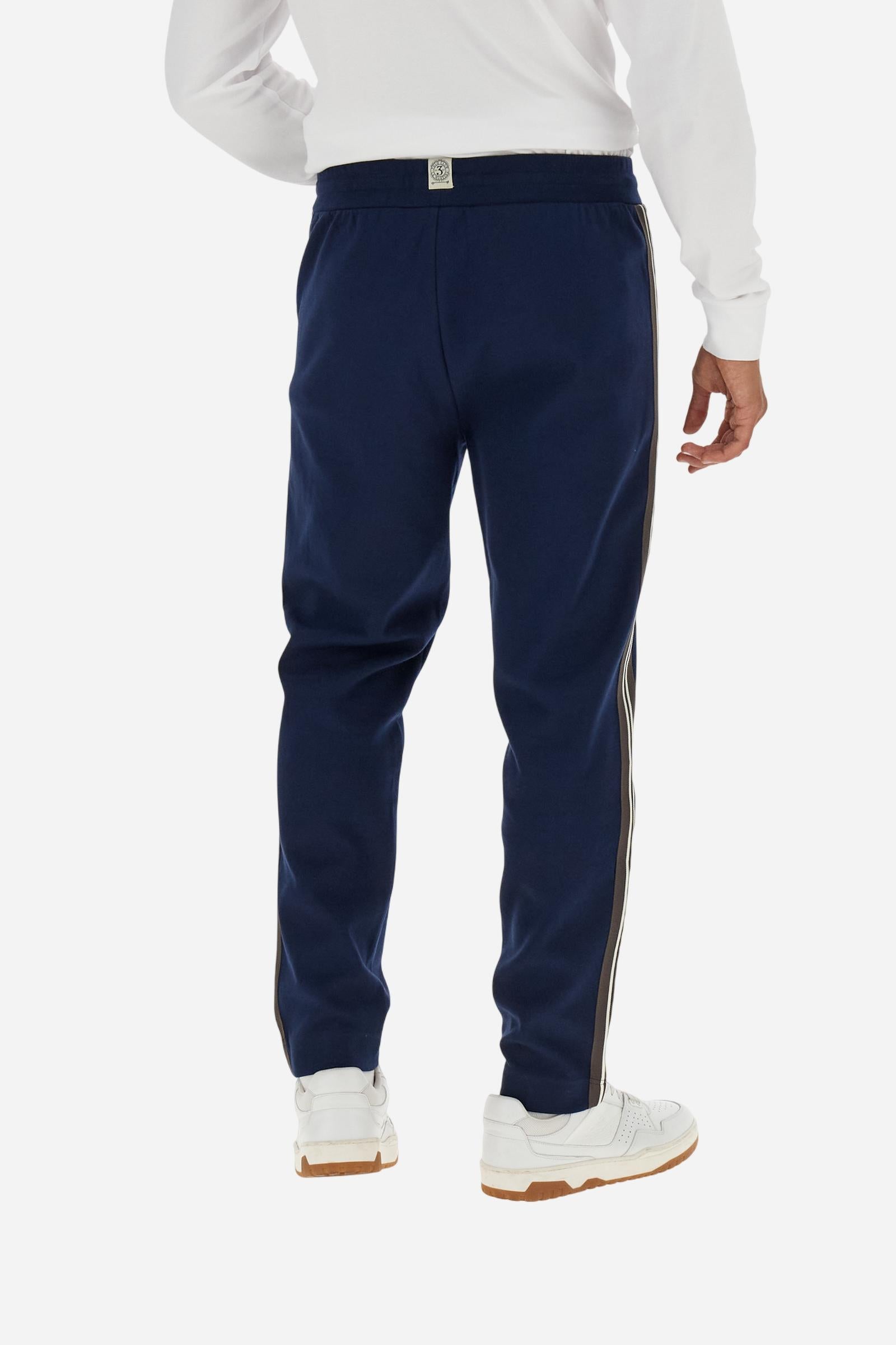 Men’s joggers made of 100% cotton interlock fleece with a bicolor design. Elastic waistband with drawstring for a customizable fit. Two zipped side pockets add practicality, while multicolor striped tape decorates both sides. A vertical crease on the front leg adds refinement to this sporty style. Small embroidered logo in contrast under the left pocket. Regular straight-leg fit for a classic, comfortable silhouette. Model wears size L. - Navy