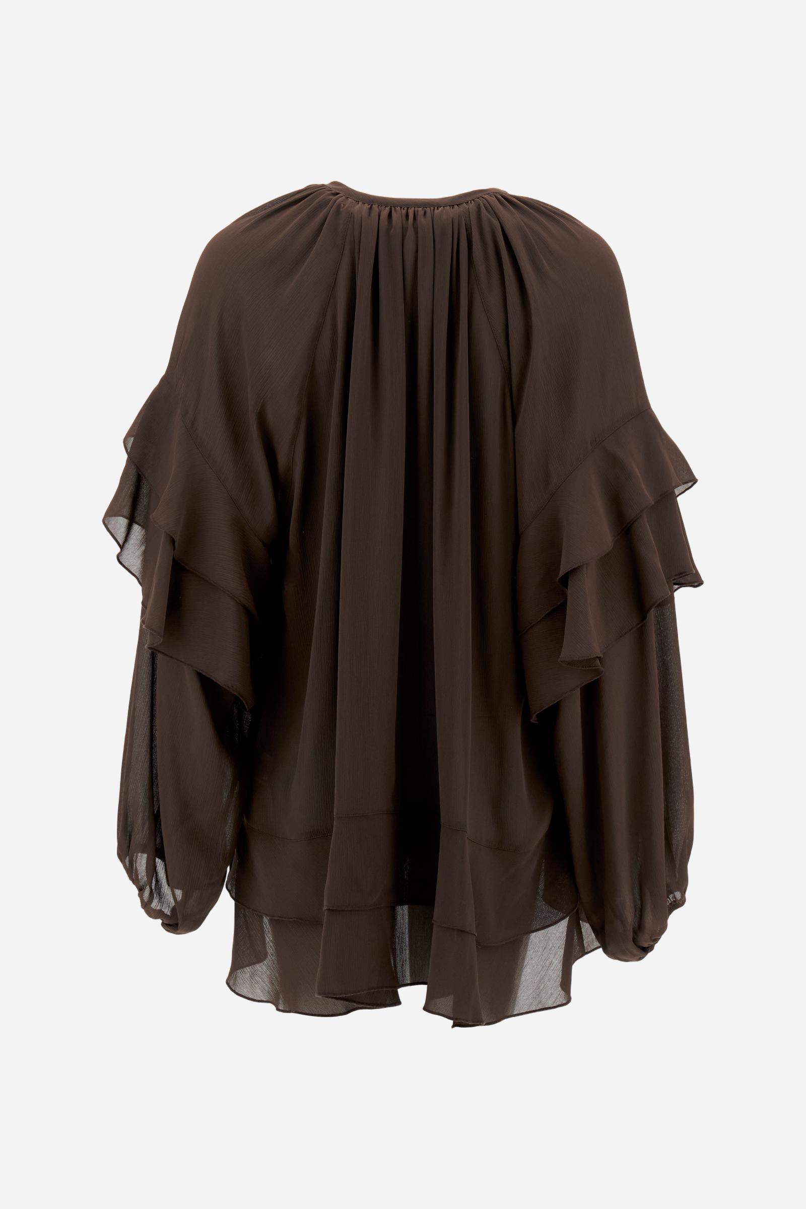 Women’s blouse with long sleeves in solid-colour chiffon with mandarin collar and V-neckline closed by ties and covered buttons. Loose fit with longer back and wide ruffles on sleeves and hem. The logo appears on a small golden metal plate applied to the front hem. The model wears size 2. - Java