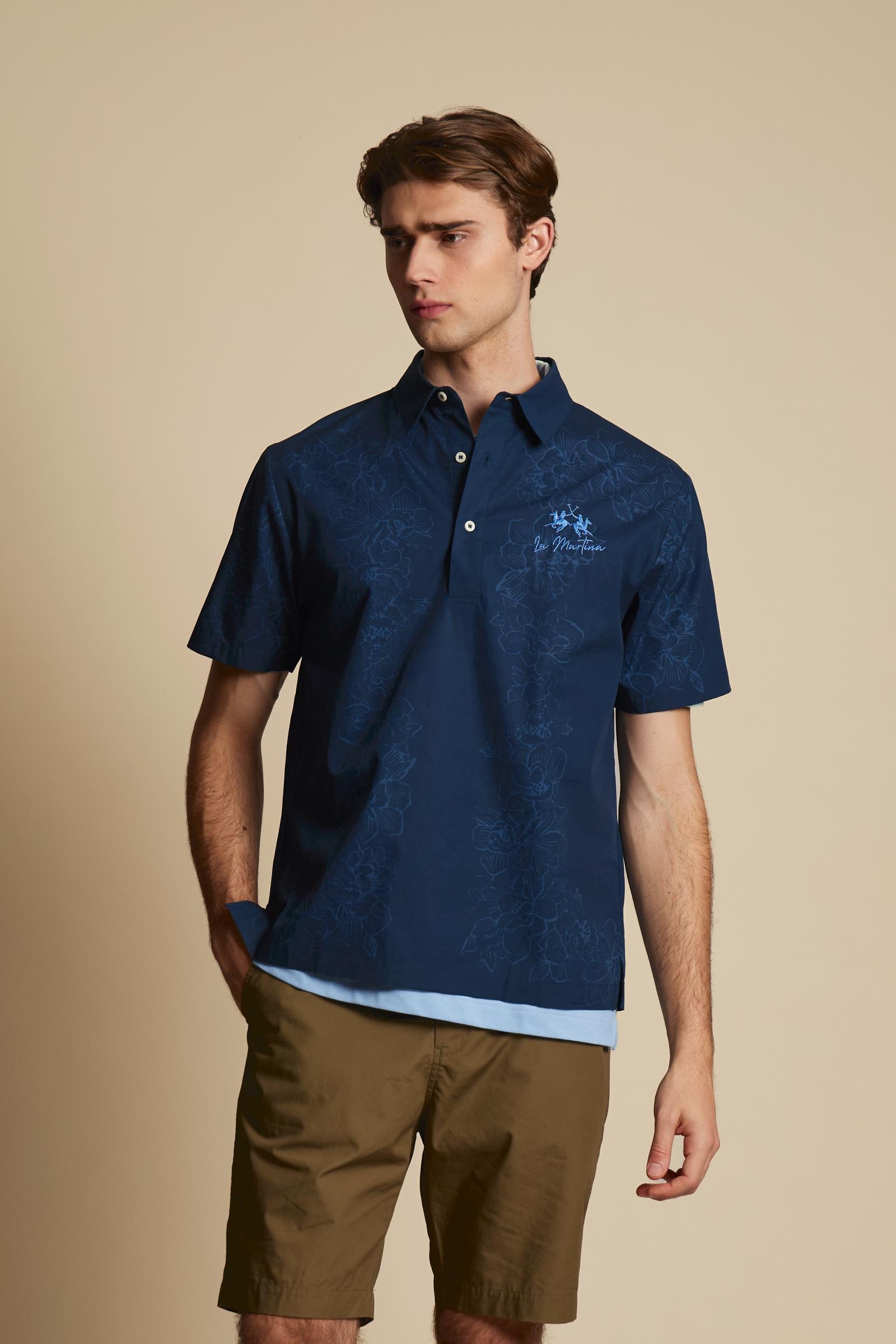 Men’s short-sleeved polo shirt made from lightweight solid-color pure cotton poplin. The contrasting floral print, with its fine graphic line, develops vertically across the front and back of the garment, adding movement to the design. The style features a classic collar and polo-style fastening with a two-button placket. The fit is comfortable, with a straight hem and short sleeves cut in a clean, roomy shape. The contrasting embroidered logo on the chest signs the garment with discretion. The model is wea
