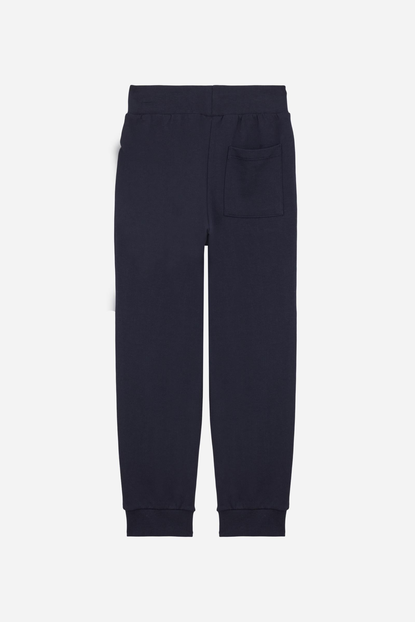 Jogger trousers for boys made from soft 100% cotton fleece in a solid colour. The style features a regular fit, a slightly tapered leg and an adjustable waist with flat drawstring. Side pockets and a patch pocket on the back add practicality, while the small contrast embroidered brand logo on the front completes the garment with a discreet, distinctive detail. - Navy
