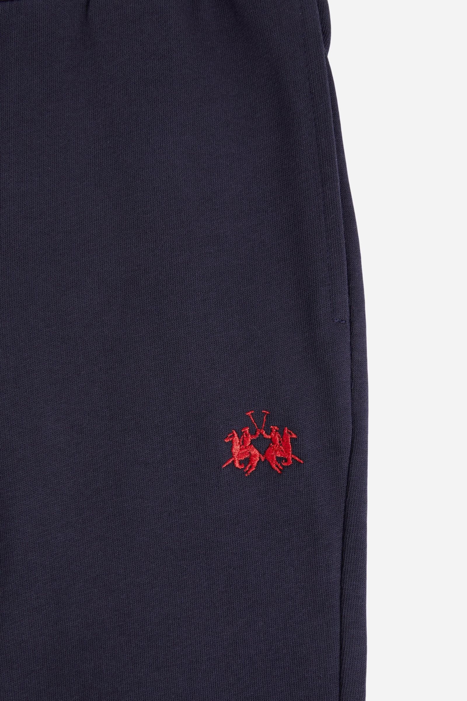 Jogger trousers for boys made from soft 100% cotton fleece in a solid colour. The style features a regular fit, a slightly tapered leg and an adjustable waist with flat drawstring. Side pockets and a patch pocket on the back add practicality, while the small contrast embroidered brand logo on the front completes the garment with a discreet, distinctive detail. - Navy