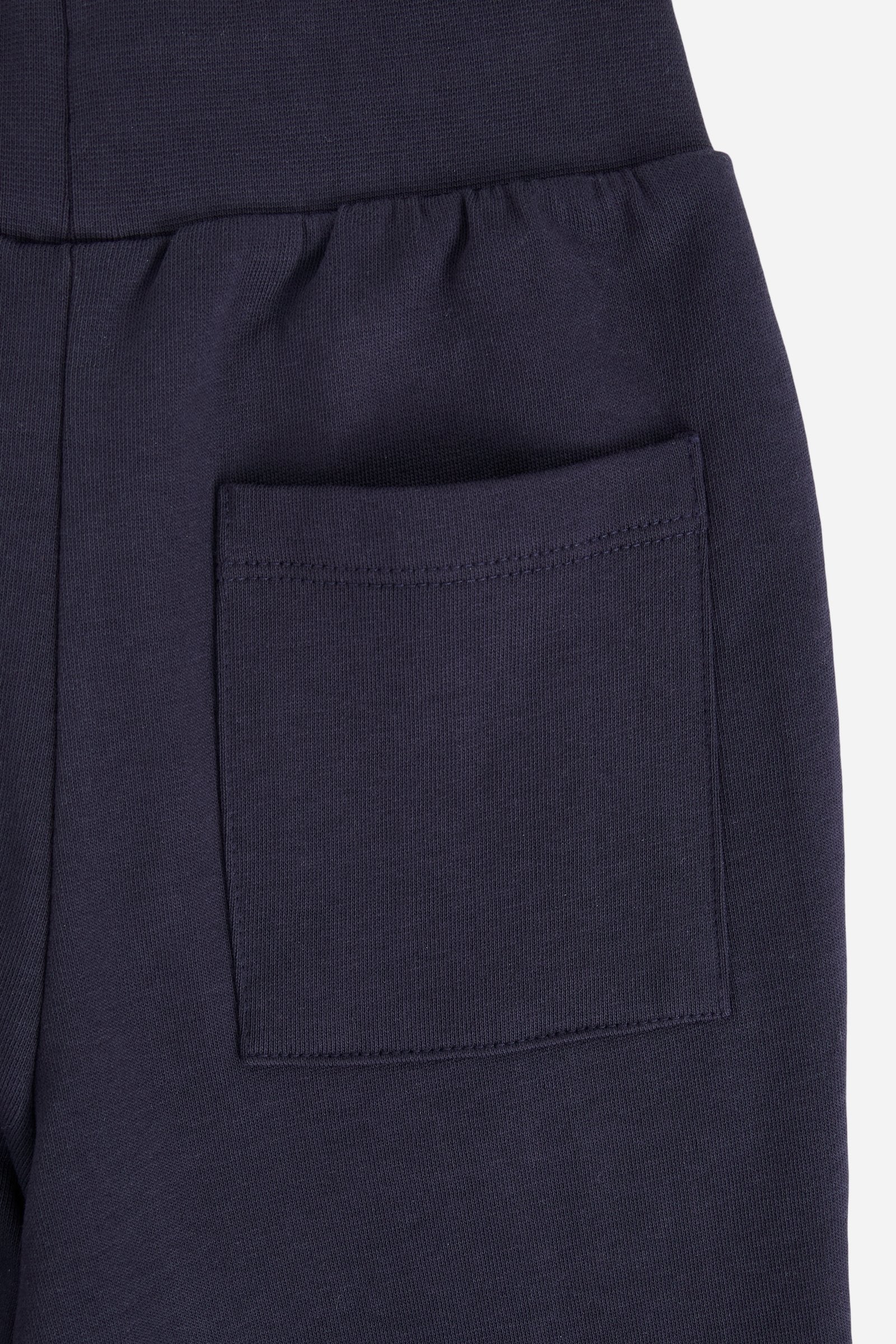 Jogger trousers for boys made from soft 100% cotton fleece in a solid colour. The style features a regular fit, a slightly tapered leg and an adjustable waist with flat drawstring. Side pockets and a patch pocket on the back add practicality, while the small contrast embroidered brand logo on the front completes the garment with a discreet, distinctive detail. - Navy
