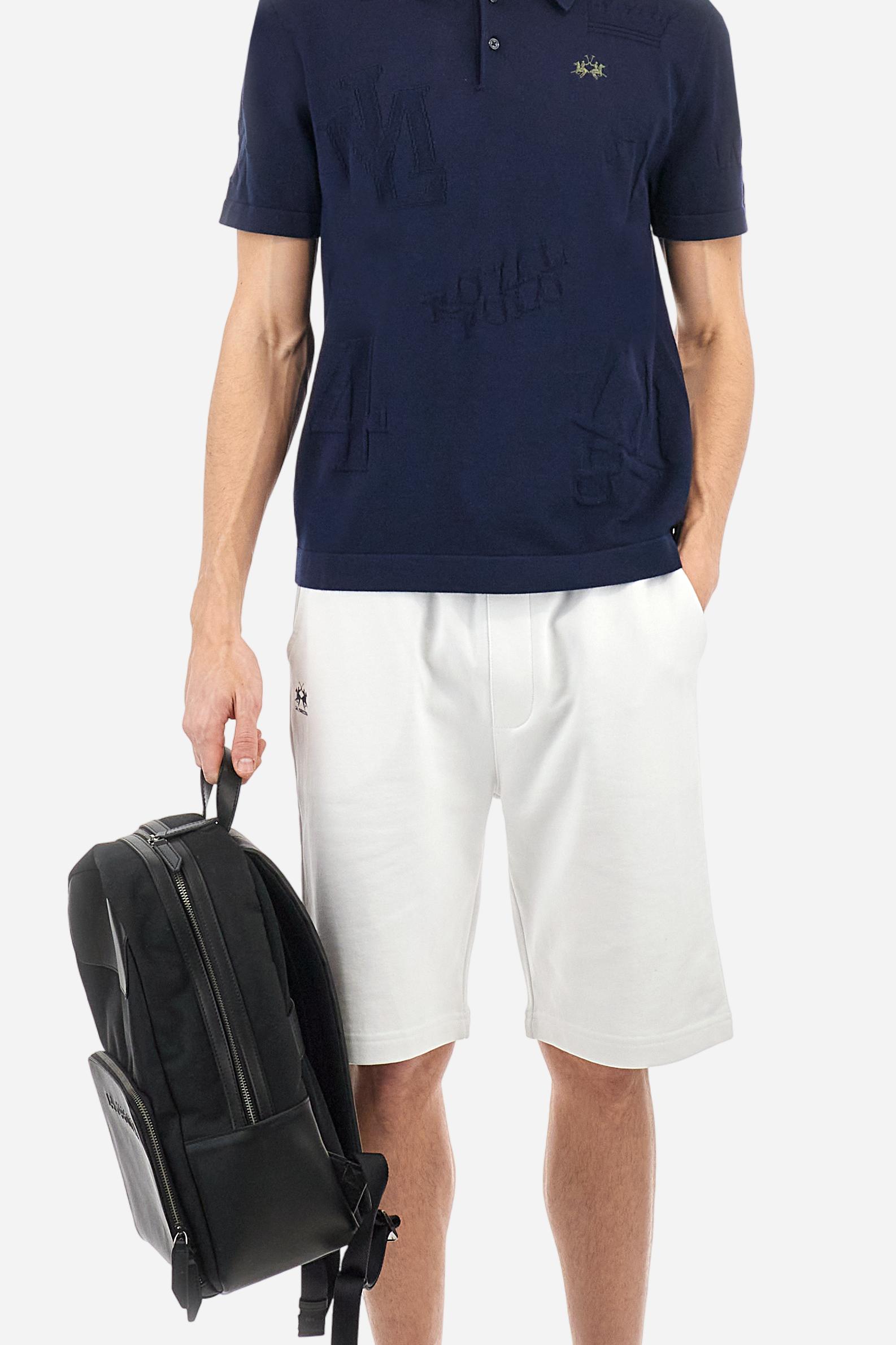 Men's short-sleeved, single-colour knitted polo shirt made of 100% combed cotton yarn. The fastening is with three buttons and the inside of the opening is in vertical rib. Various graphics are present over the garment, made by machine using an inlay technique. The logo on the left side of the chest is embroidered tone on tone. Regular fit. The model is wearing a size L. - Navy