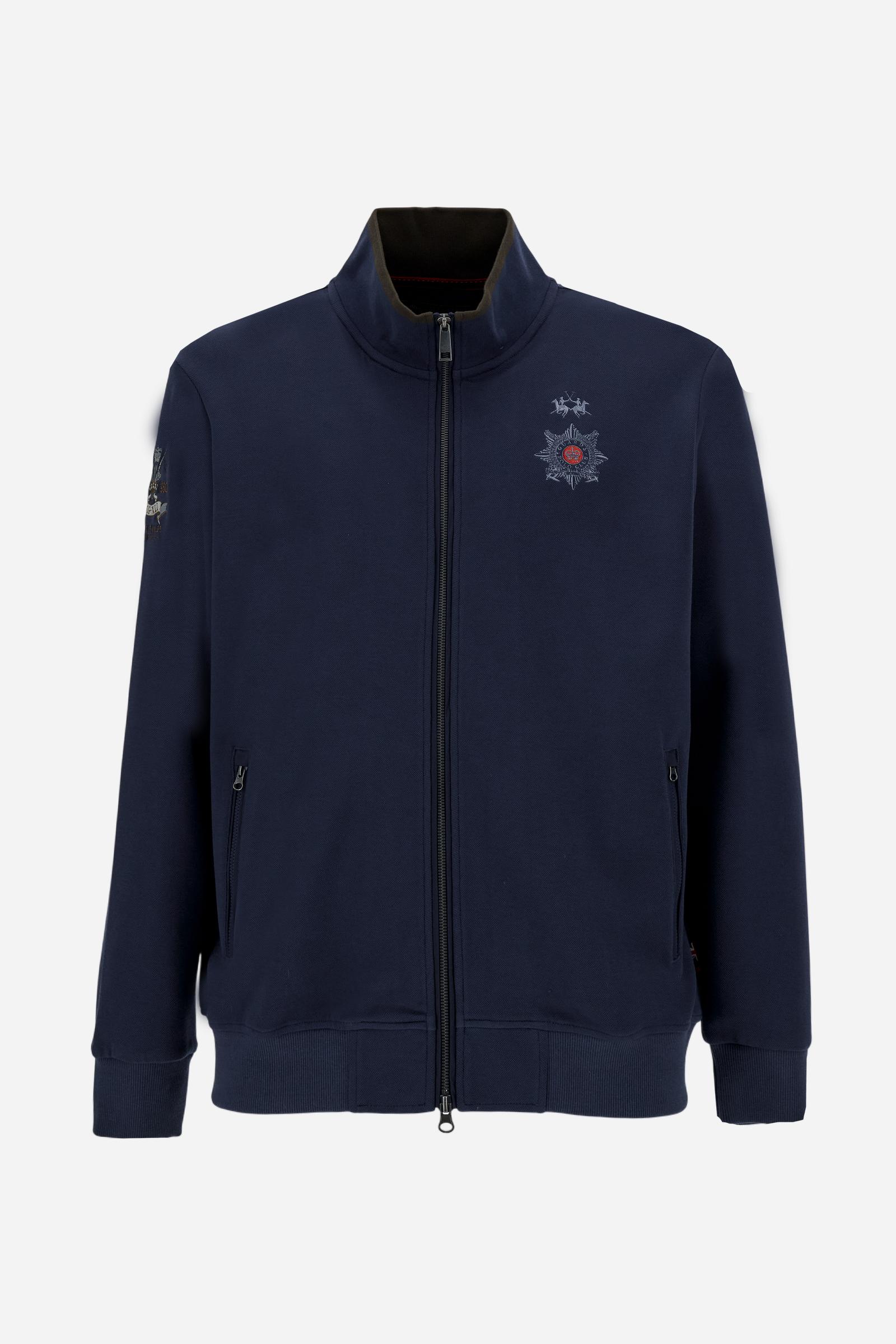 Men's long-sleeved, full-zip solid colour sweatshirt. Made of stretch cotton-blend piqué. Design with front opening fastened by a zip, high collar in two-tone ribbing. Solid colour ribbed cuffs and waistband. The small brand logo and Guards crest are embroidered in multi-coloured thread on the chest. On the right sleeve, there is another embroidery of a crest inspired by the British royal household. The regular fit silhouette is practical for everyday wear. The model is wearing a size L. - Navy