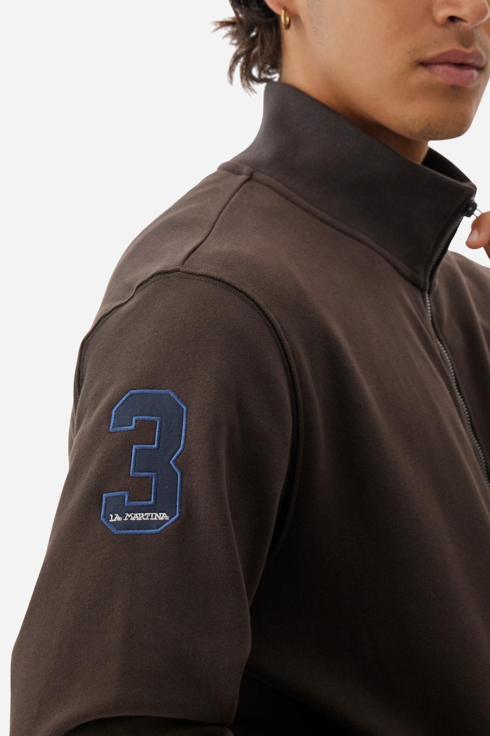 Men's long-sleeved solid colour sweatshirt. It is made of comfortable 100% cotton fleece with a soft-brushed feel. Model with high ribbed neck and front zip opening. Solid colour ribbed cuffs and waistband. The large contrasting brand team logo is embroidered on the chest. A contrasting colour fabric number patch is applied to the right sleeve. The model has a regular fit that offers a comfortable, relaxed silhouette. The model is wearing a size L. - Java