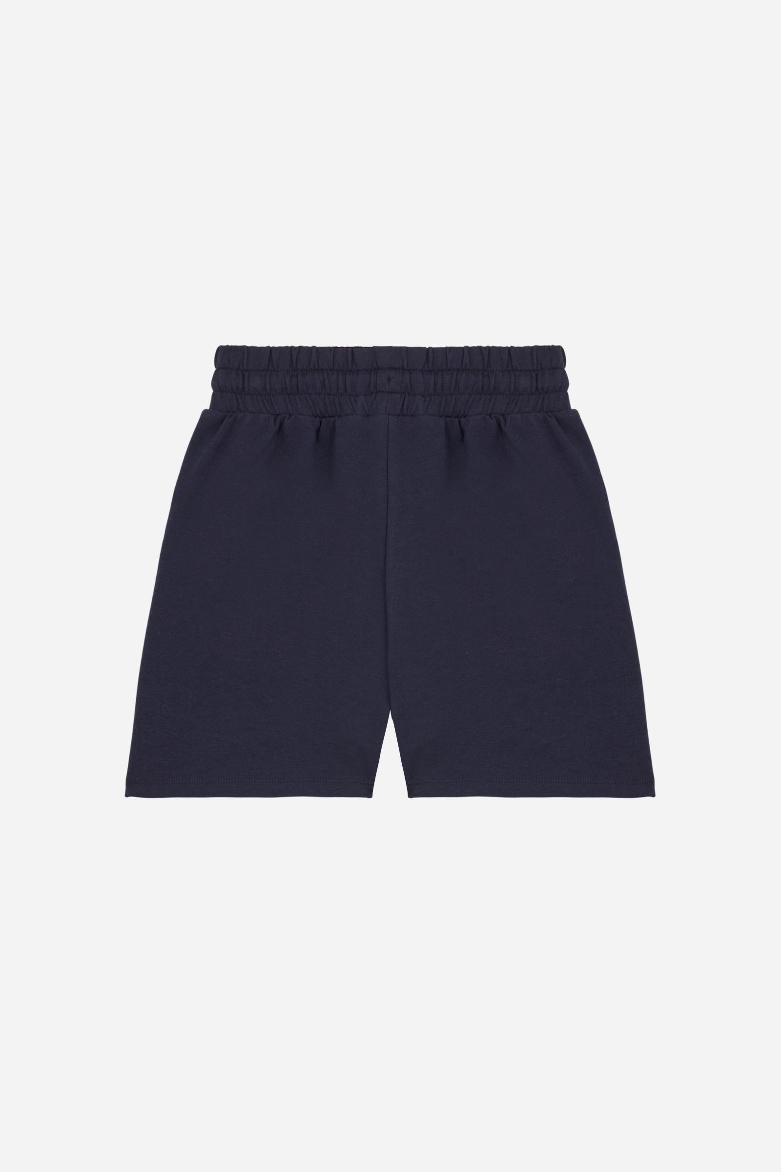Bermuda shorts for girls made from soft 100% cotton fleece in a solid colour. The style features a regular fit, short leg and elasticated waist with adjustable drawstring. The small contrast embroidered brand logo on the left leg adds a discreet and distinctive detail. A comfortable, versatile garment, ideal for casual and sporty looks. - Navy