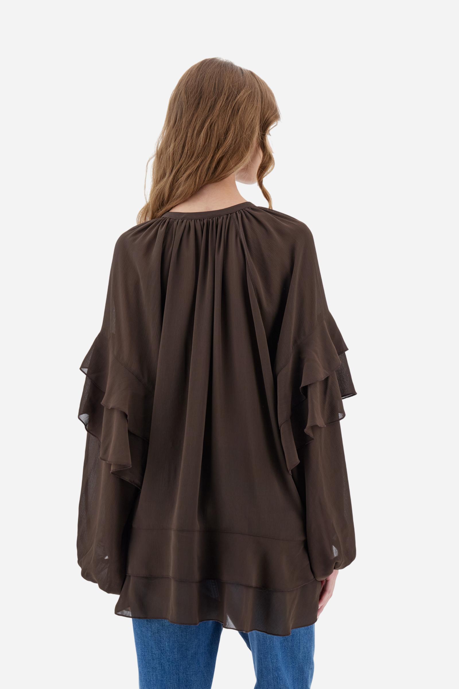 Women’s blouse with long sleeves in solid-colour chiffon with mandarin collar and V-neckline closed by ties and covered buttons. Loose fit with longer back and wide ruffles on sleeves and hem. The logo appears on a small golden metal plate applied to the front hem. The model wears size 2. - Java