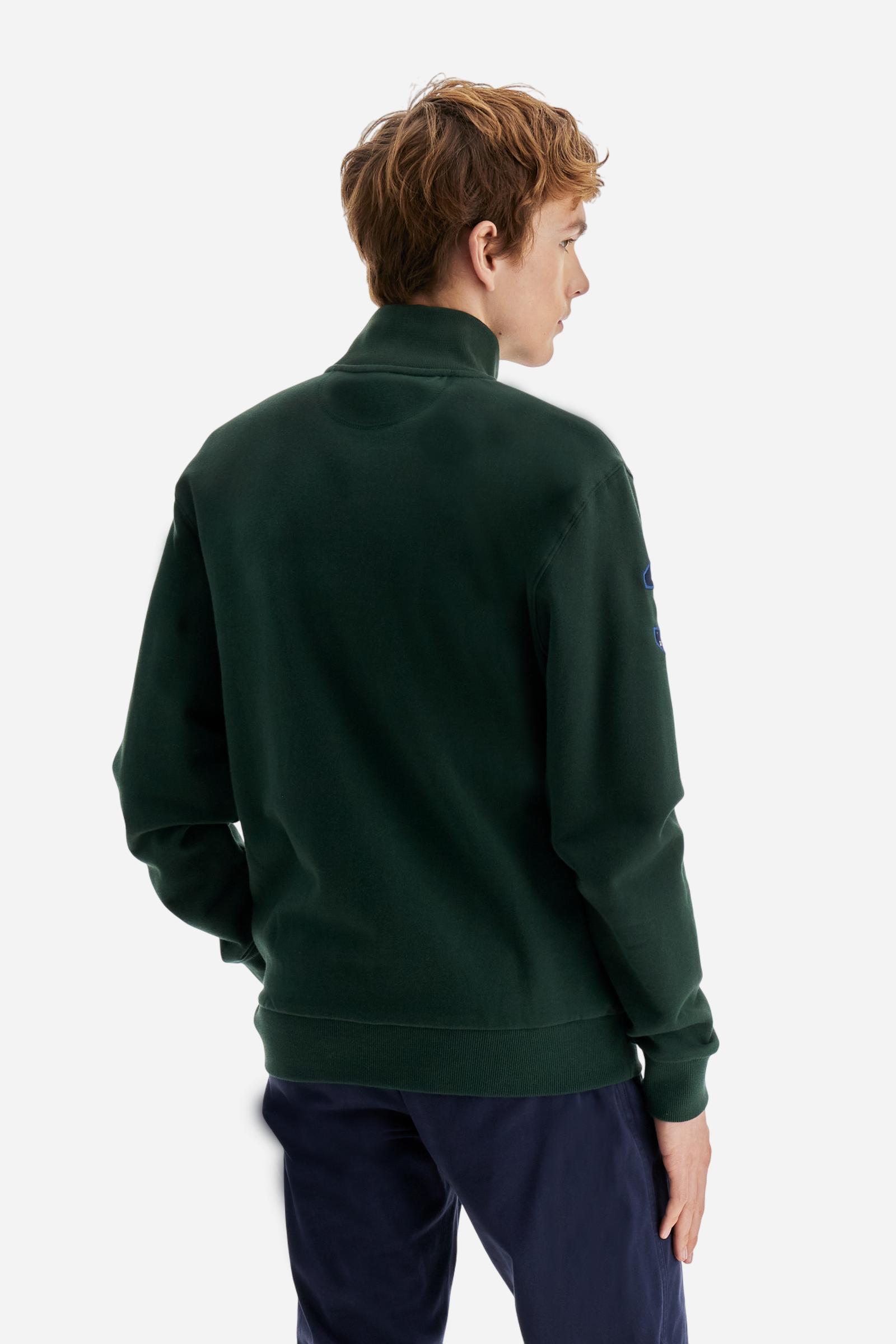 Men's long-sleeved solid colour sweatshirt. It is made of comfortable 100% cotton fleece with a soft-brushed feel. Model with high ribbed neck and front zip opening. Solid colour ribbed cuffs and waistband. The large contrasting brand team logo is embroidered on the chest. A contrasting colour fabric number patch is applied to the right sleeve. The model has a regular fit that offers a comfortable, relaxed silhouette. The model is wearing a size L. - Sycamore