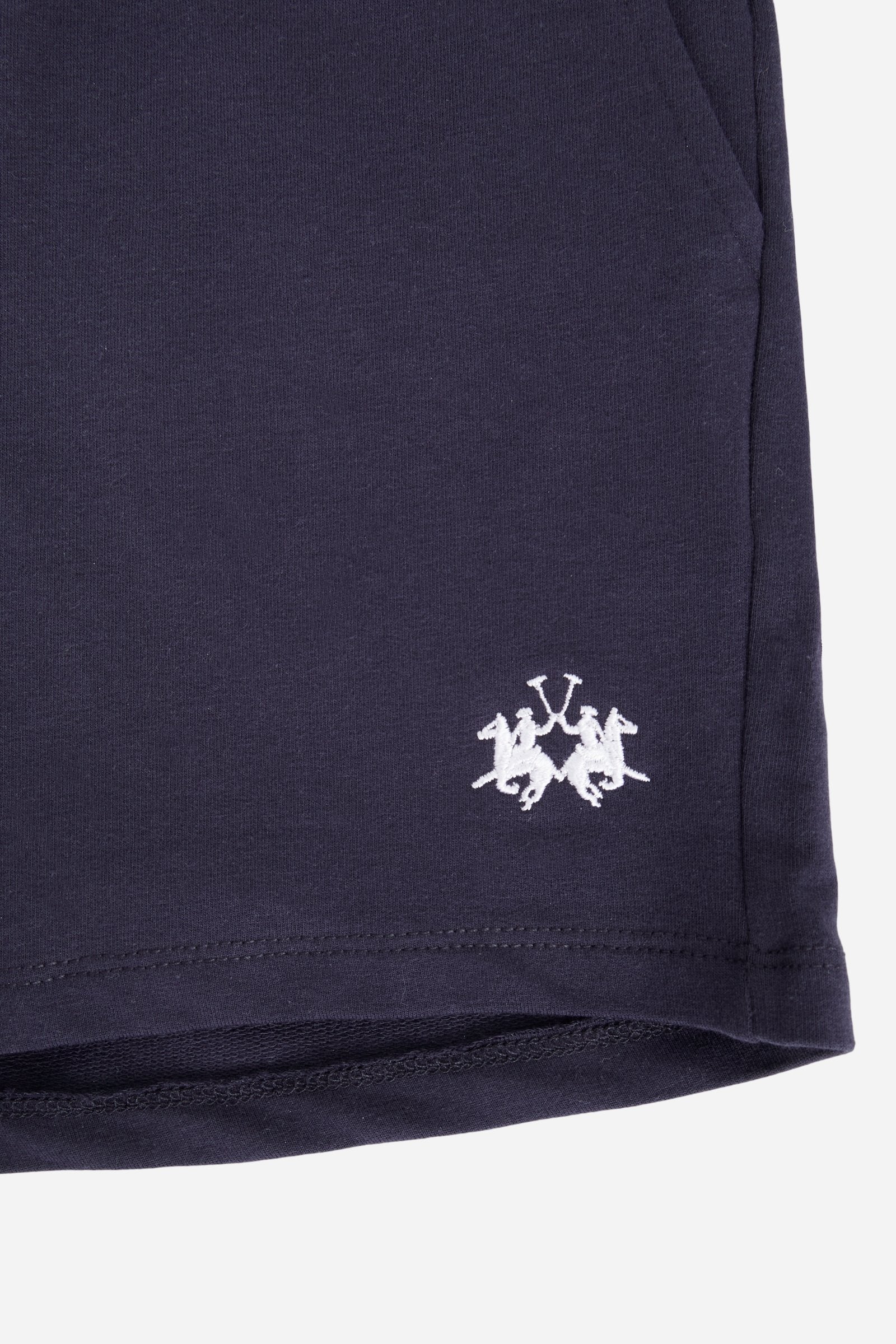 Bermuda shorts for girls made from soft 100% cotton fleece in a solid colour. The style features a regular fit, short leg and elasticated waist with adjustable drawstring. The small contrast embroidered brand logo on the left leg adds a discreet and distinctive detail. A comfortable, versatile garment, ideal for casual and sporty looks. - Navy